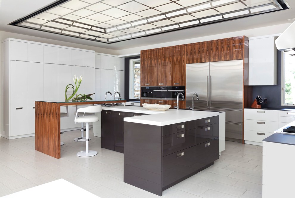 Cette image montre une cuisine américaine minimaliste en L et bois brun de taille moyenne avec un évier posé, un placard à porte plane, une crédence noire, un électroménager en acier inoxydable, un sol en linoléum et 2 îlots.