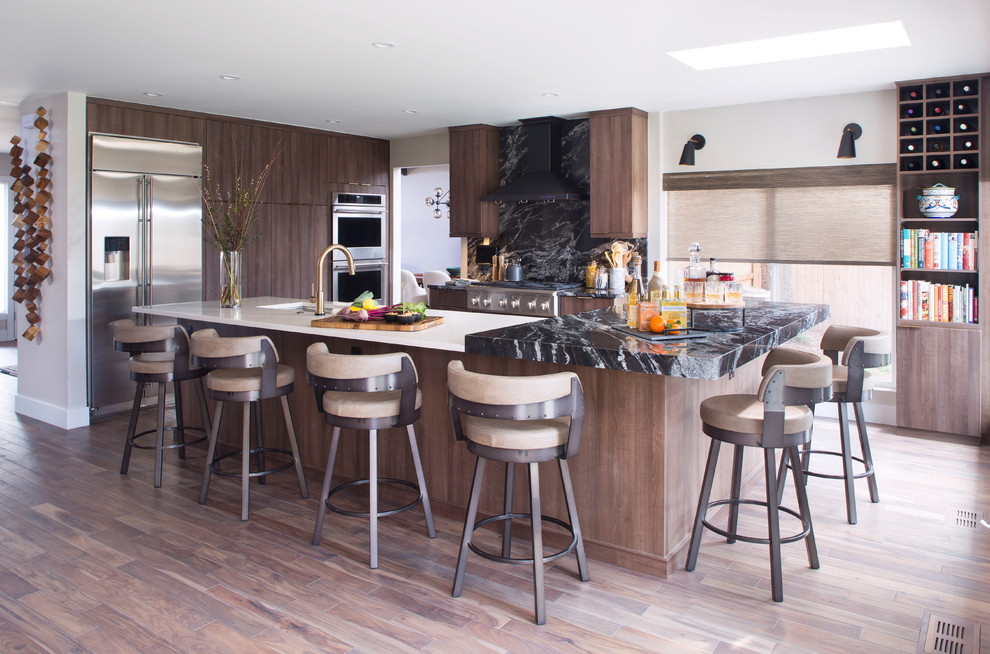 Photo of a contemporary kitchen in Denver with a submerged sink, flat-panel cabinets, dark wood cabinets, black splashback, stone slab splashback, stainless steel appliances, dark hardwood flooring, an island, brown floors and black worktops.