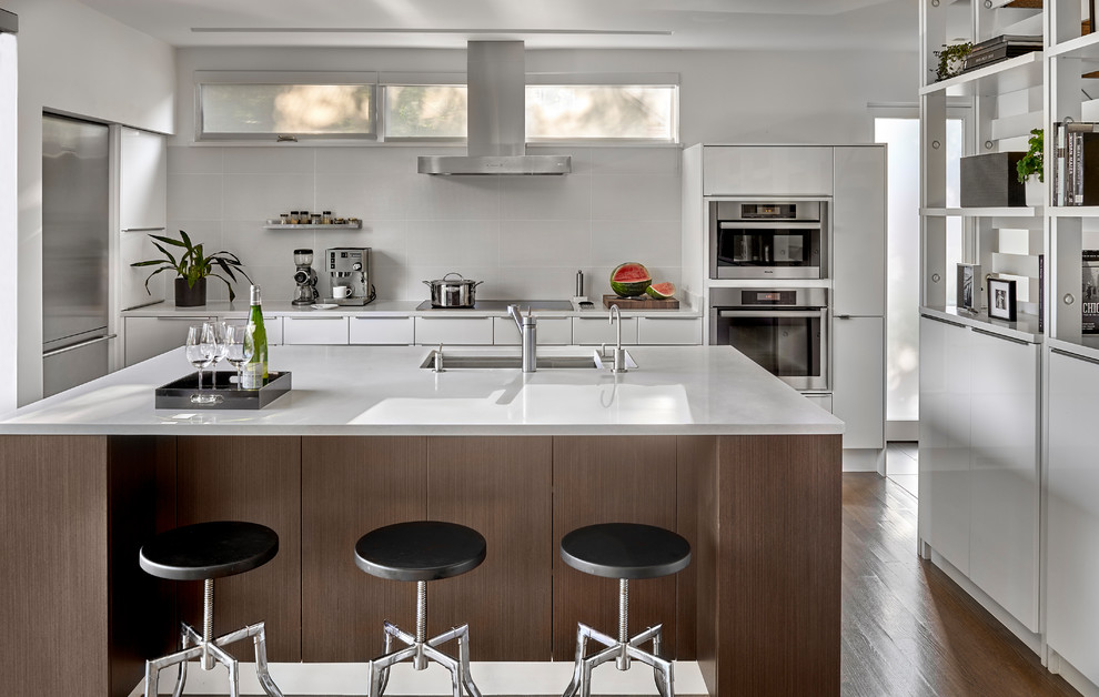 Inspiration for a mid-sized modern galley medium tone wood floor and brown floor eat-in kitchen remodel in Chicago with a single-bowl sink, flat-panel cabinets, white cabinets, quartz countertops, white backsplash, porcelain backsplash, stainless steel appliances and an island