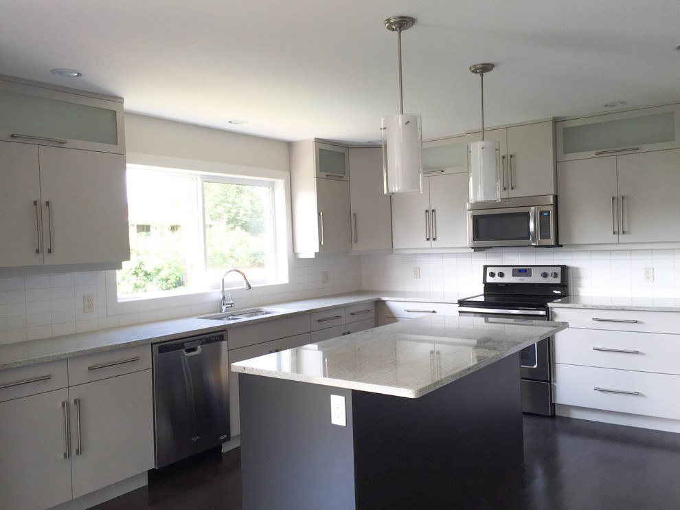 Bild på ett funkis kök, med en undermonterad diskho, släta luckor, grå skåp, granitbänkskiva, vitt stänkskydd, stänkskydd i tunnelbanekakel, rostfria vitvaror, mörkt trägolv och en köksö