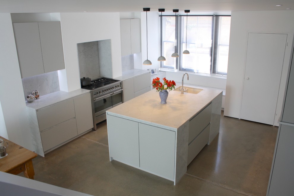 Bild på ett mellanstort funkis kök med öppen planlösning, med en undermonterad diskho, släta luckor, grå skåp, marmorbänkskiva, grått stänkskydd, stänkskydd i marmor, rostfria vitvaror, betonggolv, en köksö och grått golv