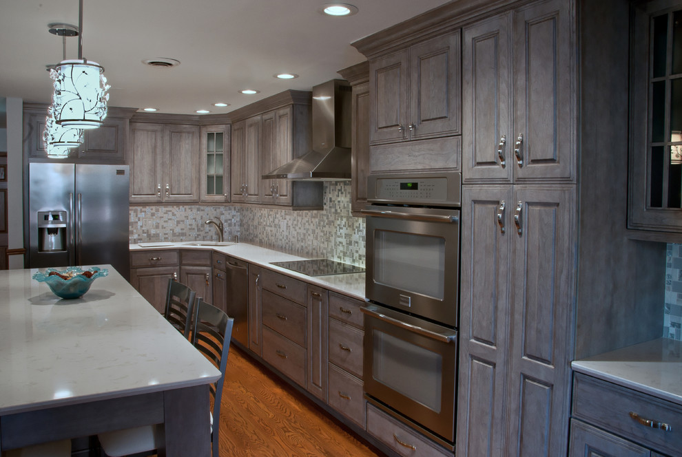 Eat-in kitchen - large transitional l-shaped medium tone wood floor and brown floor eat-in kitchen idea in Chicago with raised-panel cabinets, gray cabinets, quartz countertops, gray backsplash, mosaic tile backsplash, stainless steel appliances, an island and an undermount sink