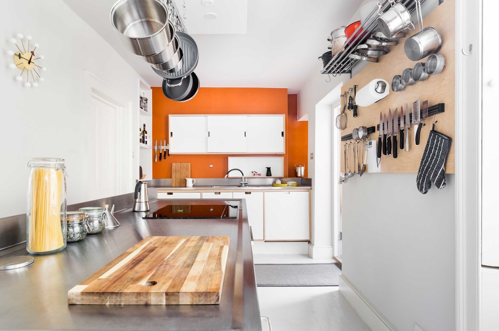 Foto på ett avskilt, mellanstort funkis u-kök, med släta luckor, vita skåp, bänkskiva i rostfritt stål, rostfria vitvaror, ljust trägolv, en köksö, vitt golv, en nedsänkt diskho och orange stänkskydd