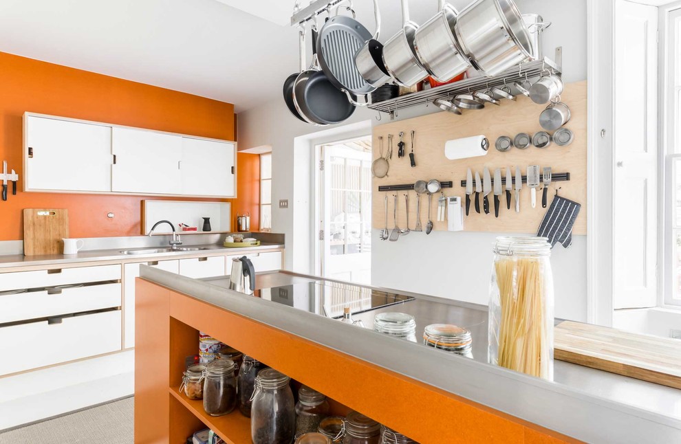 Inspiration for a medium sized contemporary u-shaped enclosed kitchen in Other with flat-panel cabinets, white cabinets, stainless steel appliances, light hardwood flooring, an island, a built-in sink, orange splashback, stainless steel worktops and white floors.