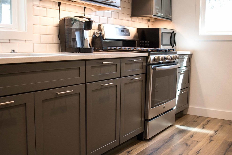 Foto på ett mellanstort funkis kök, med en undermonterad diskho, skåp i shakerstil, grå skåp, bänkskiva i kvarts, vitt stänkskydd, stänkskydd i keramik, rostfria vitvaror och laminatgolv
