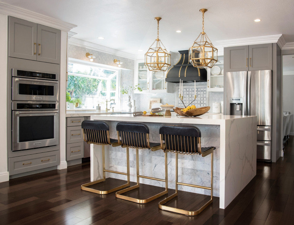 Design ideas for a classic l-shaped kitchen in Orange County with a belfast sink, shaker cabinets, grey cabinets, grey splashback, stainless steel appliances, dark hardwood flooring, an island and brown floors.