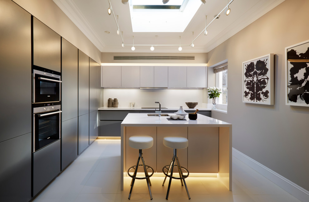 Modelo de cocinas en L gris y blanca, actual, con fregadero bajoencimera, armarios con paneles lisos, puertas de armario grises, salpicadero blanco, electrodomésticos de acero inoxidable y una isla