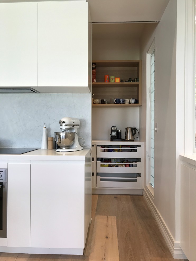 Foto på ett stort funkis kök, med en undermonterad diskho, luckor med infälld panel, vita skåp, bänkskiva i kvarts, vitt stänkskydd, stänkskydd i sten, rostfria vitvaror, ljust trägolv och en köksö