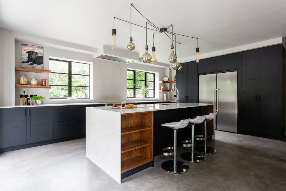 Huge transitional l-shaped gray floor open concept kitchen photo in London with raised-panel cabinets, quartz countertops, white backsplash, paneled appliances, an island, white countertops, an undermount sink and black cabinets