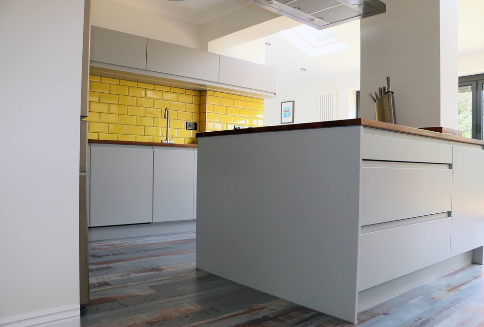 Foto på ett funkis kök och matrum, med grå skåp, träbänkskiva, gult stänkskydd och en köksö