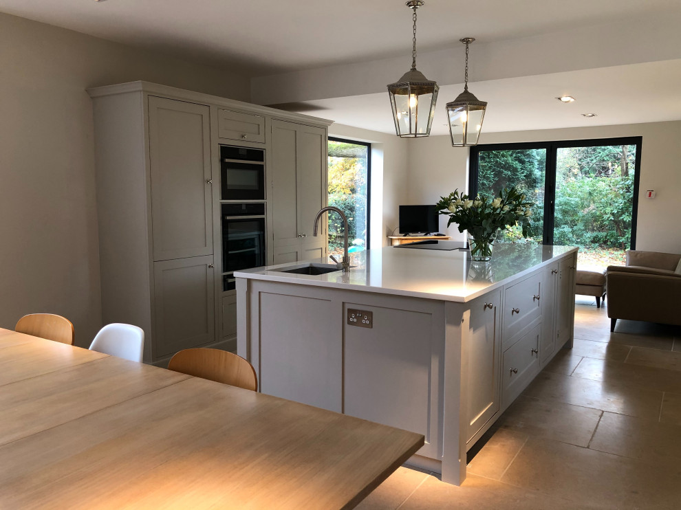 Large traditional single-wall kitchen/diner in Surrey with a built-in sink, beaded cabinets, grey cabinets, quartz worktops, grey splashback, black appliances, an island and white worktops.