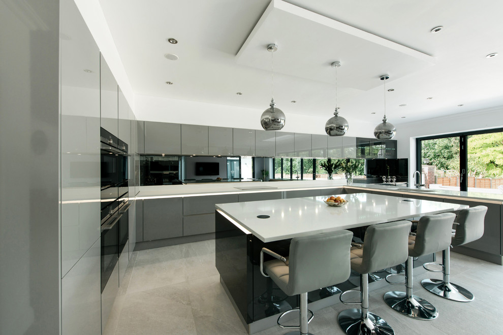 Inspiration for a large contemporary u-shaped kitchen in London with flat-panel cabinets, grey cabinets, mirror splashback, an island, grey floors, white worktops, a submerged sink and black appliances.