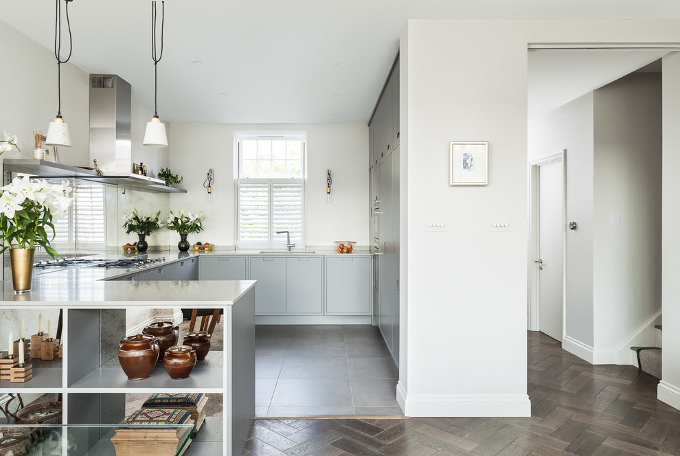Bild på ett funkis u-kök, med släta luckor, grå skåp, vitt stänkskydd, rostfria vitvaror och grått golv
