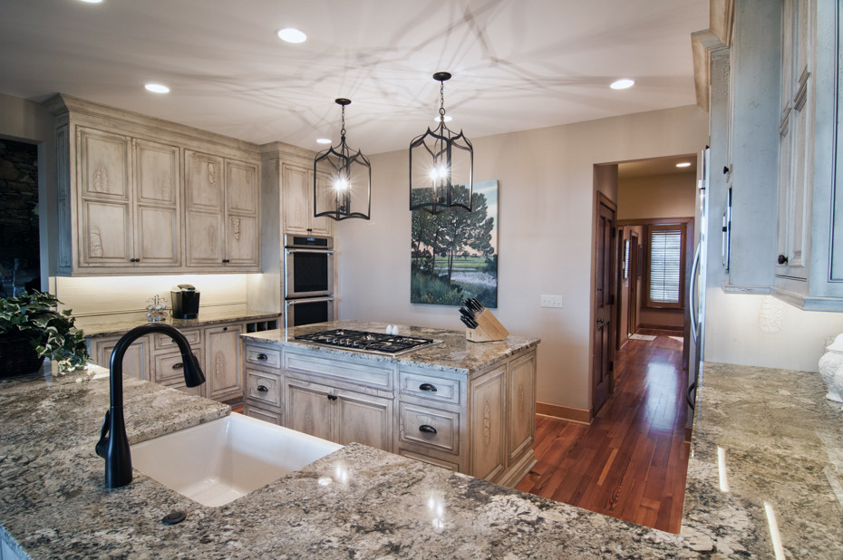 Example of a mid-sized transitional u-shaped medium tone wood floor and beige floor enclosed kitchen design in Charleston with a farmhouse sink, distressed cabinets, granite countertops, beige backsplash, stainless steel appliances and an island