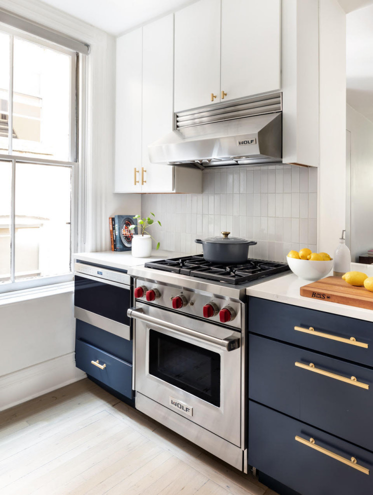 Example of a small transitional galley light wood floor and beige floor enclosed kitchen design in New York with blue cabinets, gray backsplash, ceramic backsplash, stainless steel appliances, no island and white countertops