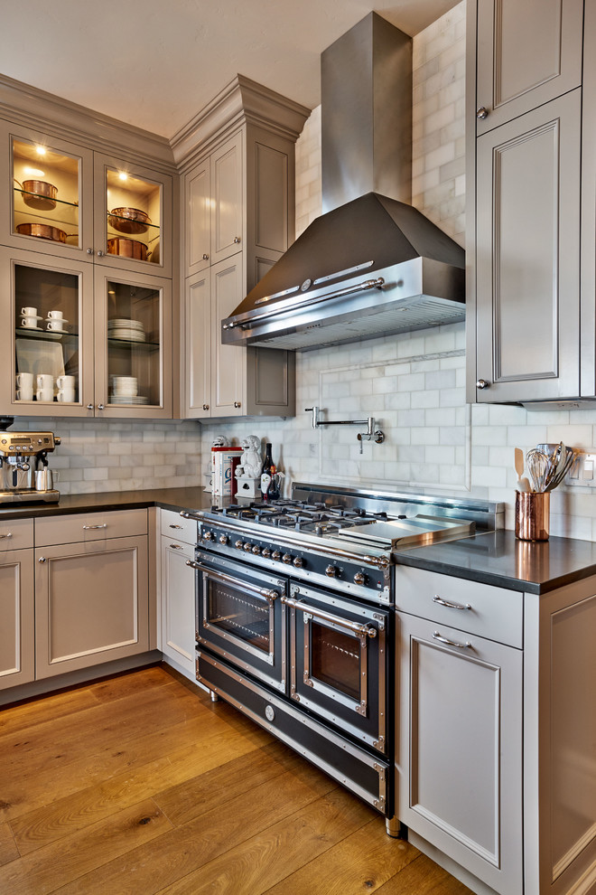 Enclosed kitchen - mid-sized traditional u-shaped light wood floor enclosed kitchen idea in Portland with a farmhouse sink, recessed-panel cabinets, gray cabinets, quartz countertops, white backsplash, stone tile backsplash, black appliances and an island