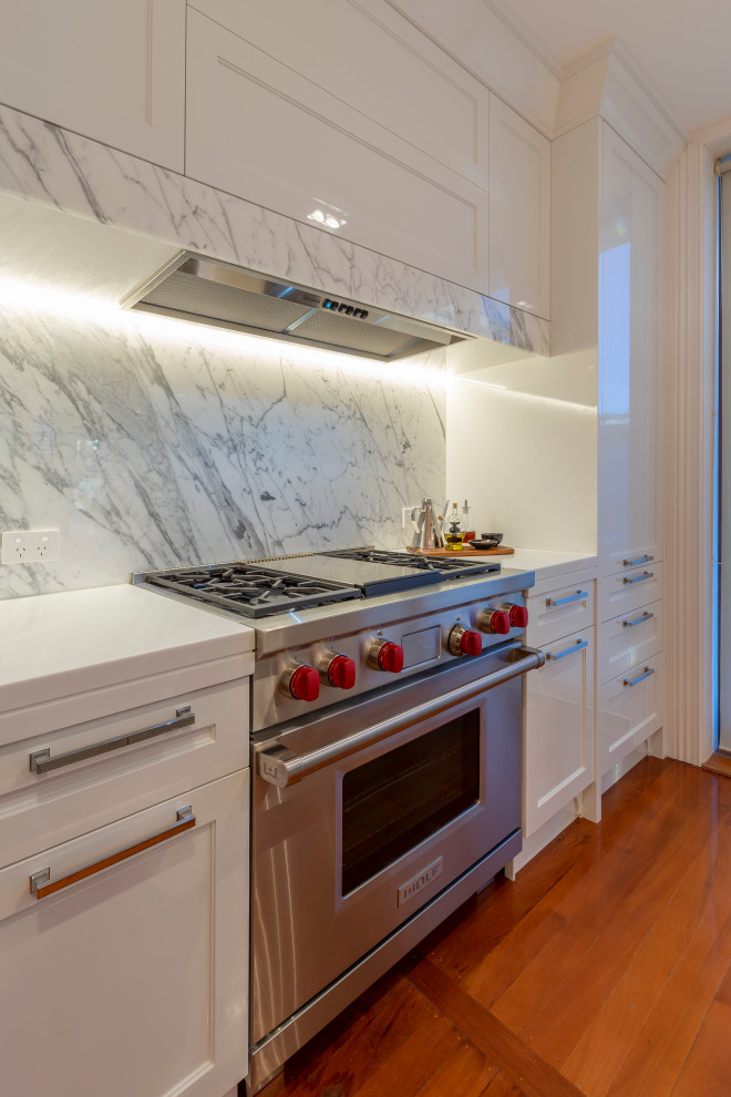 Foto på ett mellanstort vintage vit linjärt kök och matrum, med en undermonterad diskho, luckor med infälld panel, vita skåp, bänkskiva i koppar, grått stänkskydd, stänkskydd i marmor, rostfria vitvaror, mellanmörkt trägolv, en köksö och brunt golv