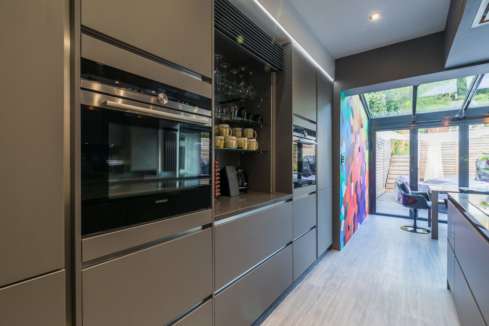 Contemporary kitchen in London with flat-panel cabinets, grey cabinets, quartz worktops, black appliances, a breakfast bar and grey worktops.