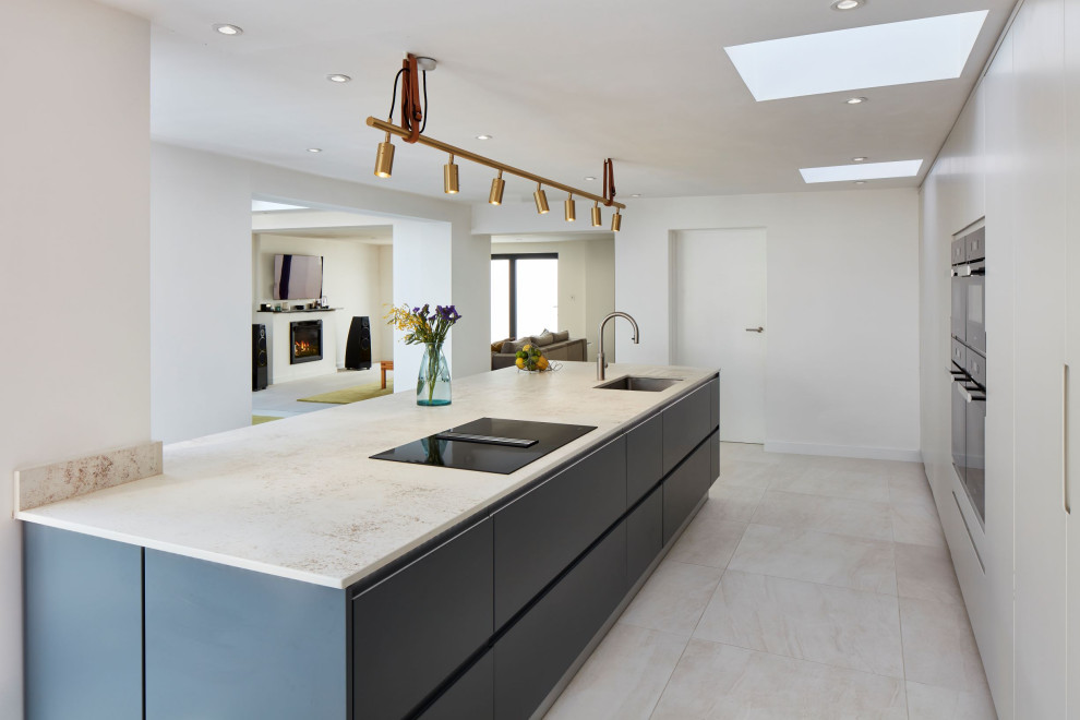 This is an example of a large contemporary single-wall kitchen in London with recessed-panel cabinets, grey cabinets, stainless steel appliances, an island, multi-coloured floors and white worktops.