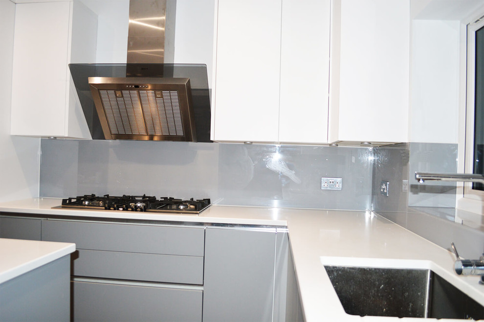 ハートフォードシャーにあるラグジュアリーな広いモダンスタイルのおしゃれなキッチン (フラットパネル扉のキャビネット、白いキャビネット、ライムストーンカウンター、グレーのキッチンパネル、ガラス板のキッチンパネル) の写真