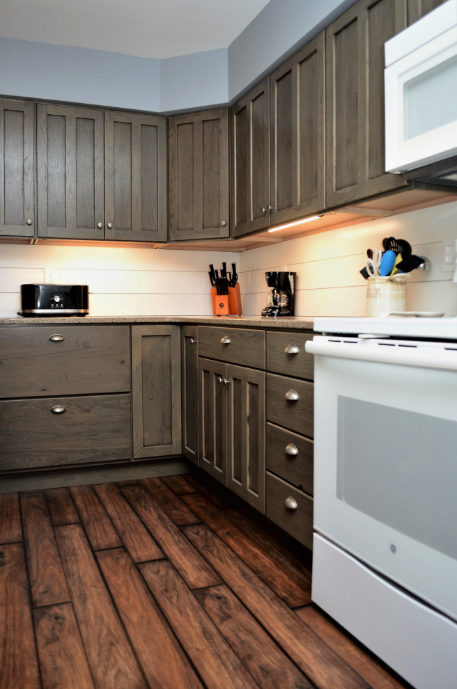 Bild på ett mellanstort rustikt brun brunt kök, med en rustik diskho, luckor med infälld panel, grå skåp, bänkskiva i kvartsit, vitt stänkskydd, vita vitvaror, laminatgolv, en halv köksö och brunt golv