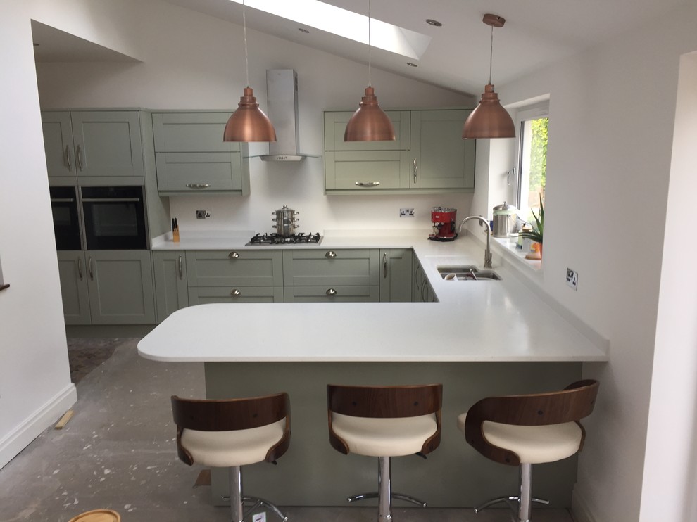 Photo of a medium sized classic u-shaped kitchen/diner in Cardiff with a submerged sink, shaker cabinets, green cabinets, quartz worktops, white splashback, window splashback, stainless steel appliances, concrete flooring, a breakfast bar, grey floors and white worktops.