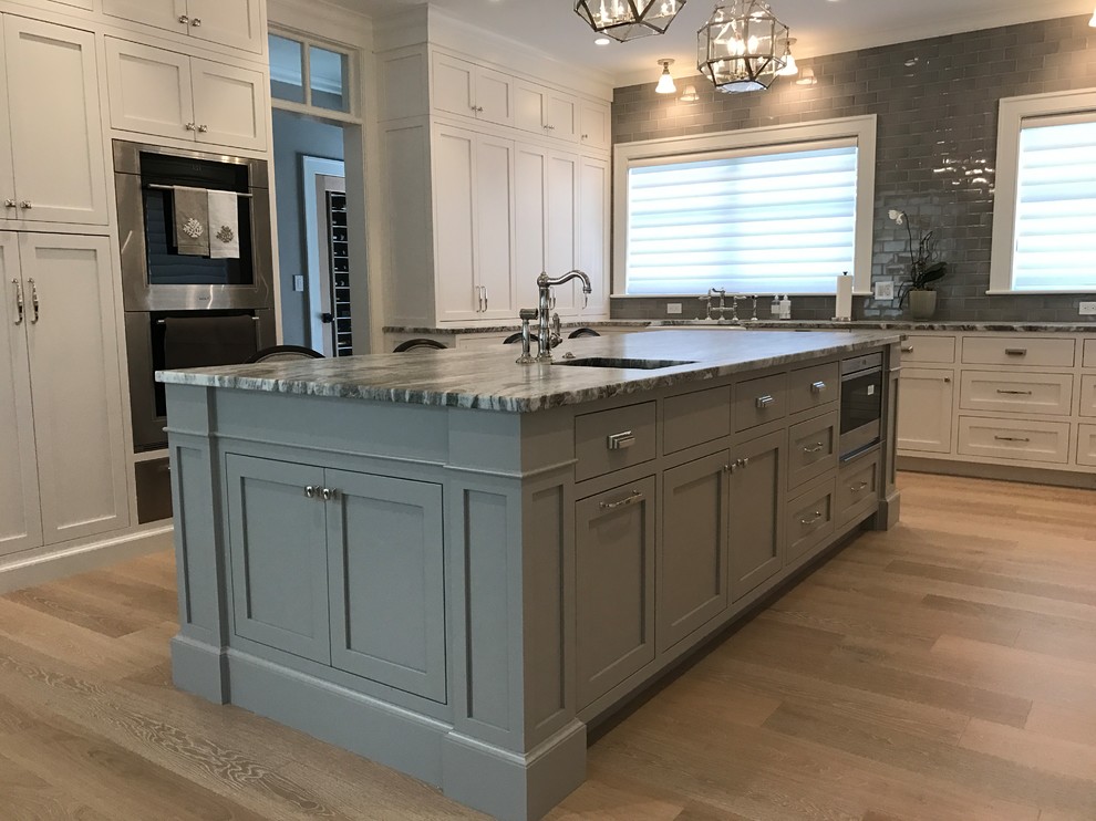 Inspiration for a large transitional u-shaped medium tone wood floor and brown floor enclosed kitchen remodel in Boston with a farmhouse sink, shaker cabinets, white cabinets, granite countertops, gray backsplash, subway tile backsplash, paneled appliances, an island and gray countertops