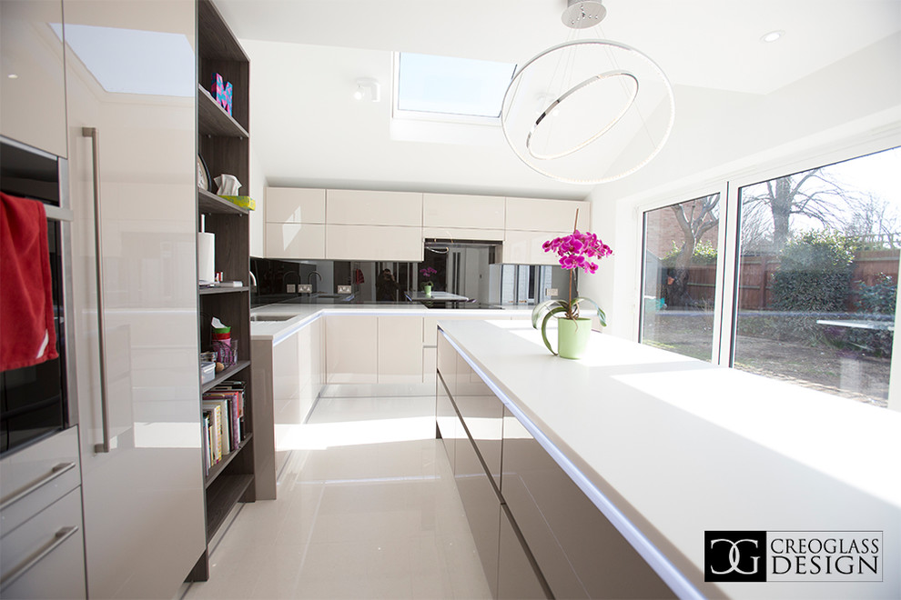 Photo of a large modern kitchen/diner in Hertfordshire with flat-panel cabinets, beige cabinets, marble worktops, grey splashback, glass sheet splashback and an island.