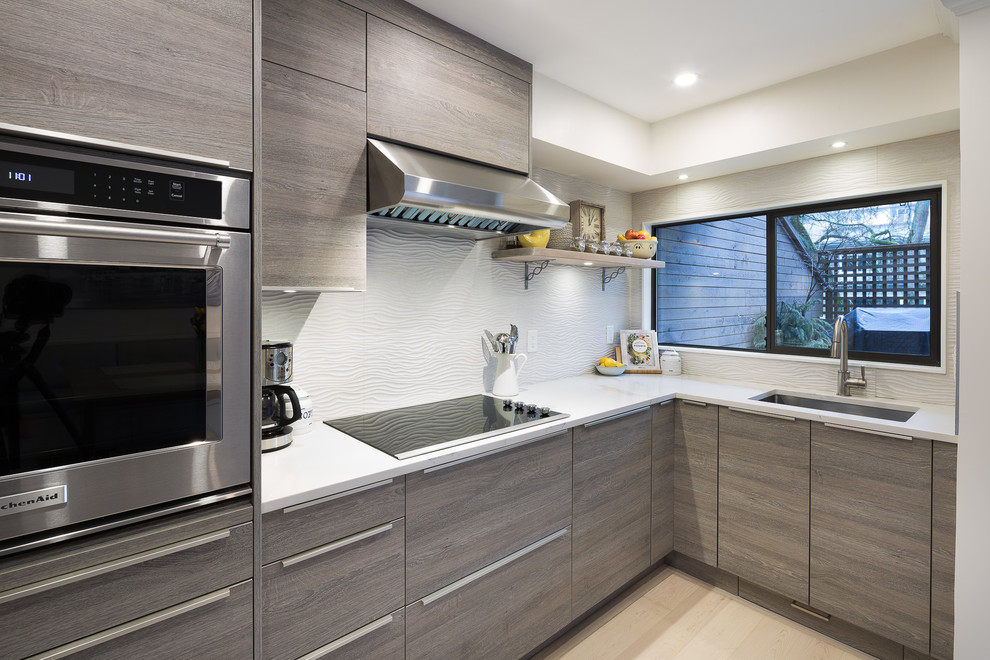 Photo of a small contemporary l-shaped kitchen/diner in Vancouver with a submerged sink, flat-panel cabinets, quartz worktops, white splashback, porcelain splashback, stainless steel appliances, light hardwood flooring, no island, grey cabinets and beige floors.