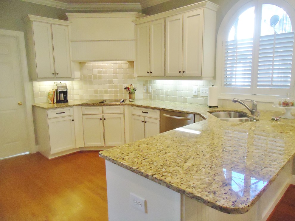 Example of a classic u-shaped medium tone wood floor kitchen design in Birmingham with an undermount sink, shaker cabinets, white cabinets, granite countertops, beige backsplash, stone tile backsplash and stainless steel appliances