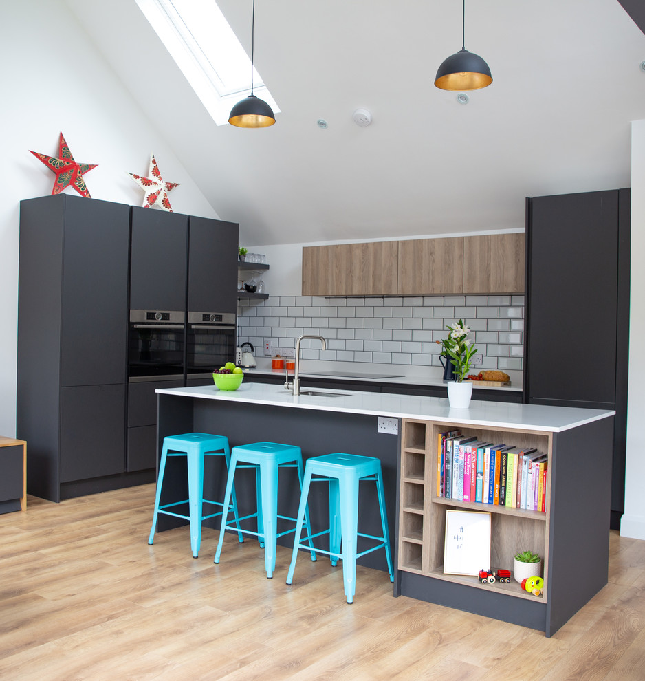 Photo of a medium sized modern l-shaped open plan kitchen in Other with a single-bowl sink, flat-panel cabinets, grey cabinets, quartz worktops, white splashback, ceramic splashback, integrated appliances, laminate floors, an island, brown floors and white worktops.