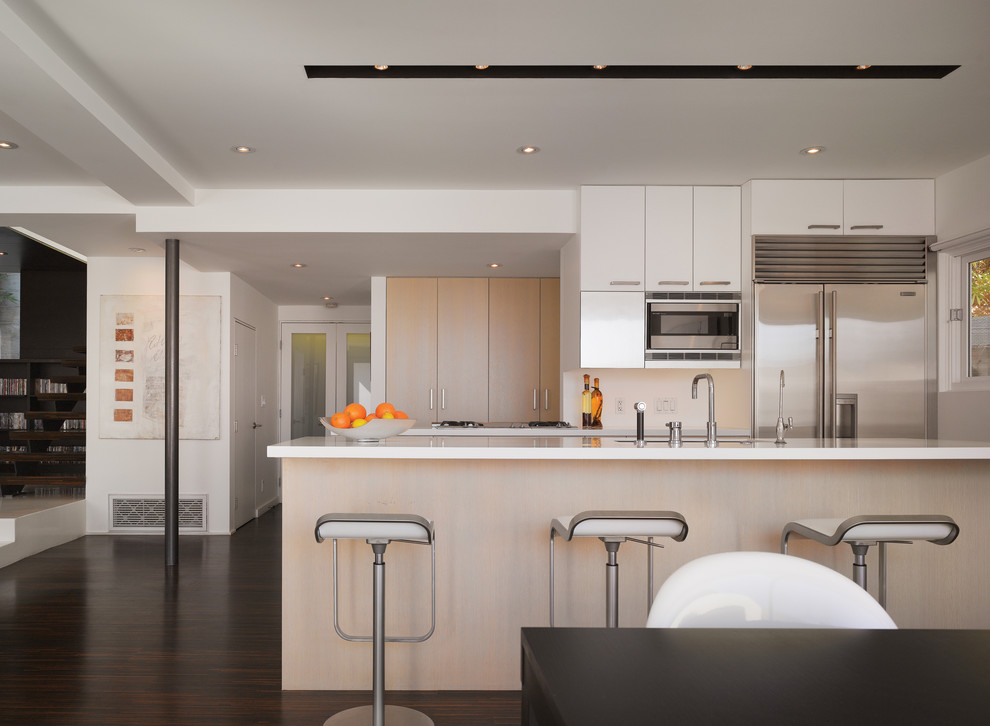 Inspiration for a small modern galley dark wood floor eat-in kitchen remodel in Los Angeles with stainless steel appliances, flat-panel cabinets, light wood cabinets, an undermount sink, solid surface countertops, white backsplash and an island