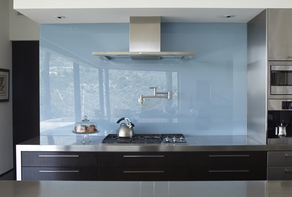 Inspiration for a mid-sized modern galley medium tone wood floor eat-in kitchen remodel in Los Angeles with glass sheet backsplash, blue backsplash, flat-panel cabinets, dark wood cabinets, stainless steel countertops, stainless steel appliances and an island