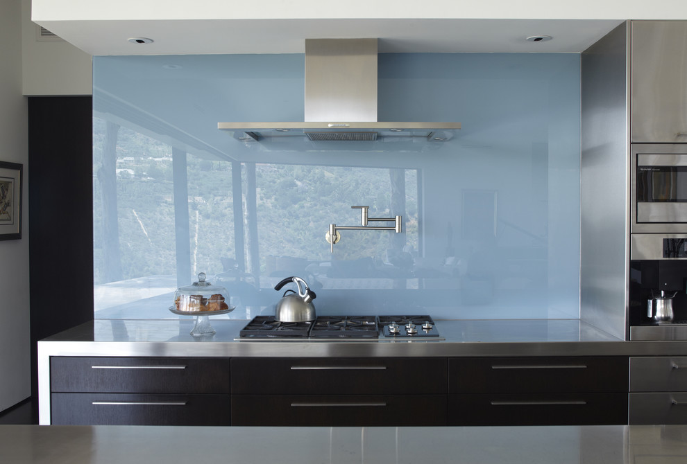 Zweizeilige, Mittelgroße Moderne Wohnküche mit Glasrückwand, Küchenrückwand in Blau, flächenbündigen Schrankfronten, dunklen Holzschränken, Edelstahl-Arbeitsplatte, Küchengeräten aus Edelstahl, braunem Holzboden und Kücheninsel in Los Angeles