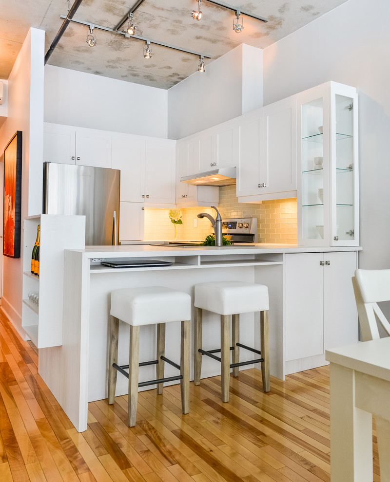 Cette image montre une cuisine américaine traditionnelle en U avec un placard à porte shaker, des portes de placard blanches, un électroménager en acier inoxydable, un sol en bois brun et une péninsule.
