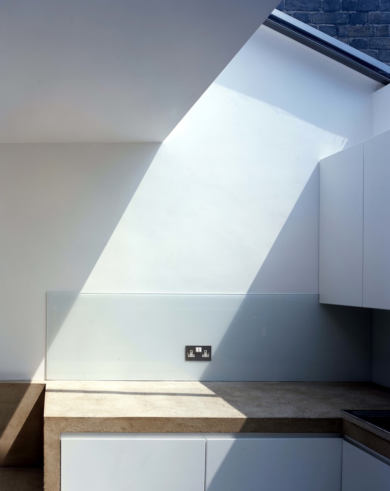 Modern inredning av ett kök, med släta luckor, vita skåp, bänkskiva i betong och glaspanel som stänkskydd