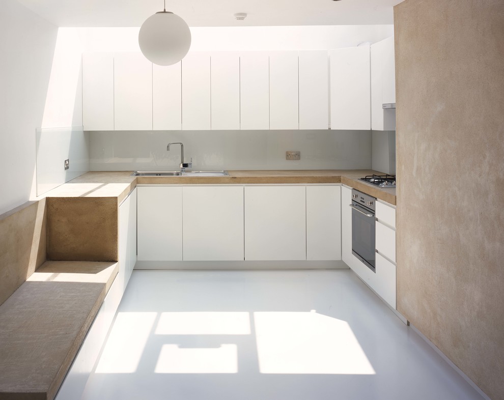 Foto på ett mellanstort funkis kök, med en nedsänkt diskho, släta luckor, vita skåp, bänkskiva i betong, vitt stänkskydd, glaspanel som stänkskydd, rostfria vitvaror och linoleumgolv