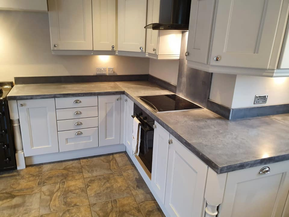 This is an example of a rural kitchen in Other with white cabinets, concrete worktops, grey splashback, stone slab splashback, black appliances and grey worktops.