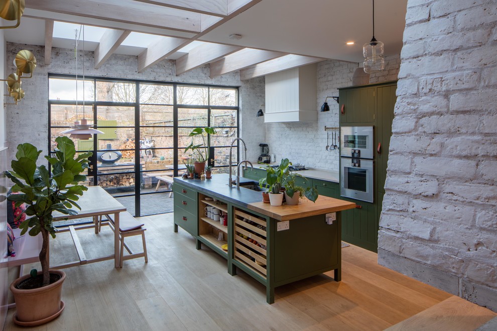 Exempel på ett skandinaviskt linjärt kök med öppen planlösning, med en dubbel diskho, skåp i shakerstil, gröna skåp, bänkskiva i kalksten, vitt stänkskydd, stänkskydd i tegel, integrerade vitvaror, mellanmörkt trägolv och en köksö