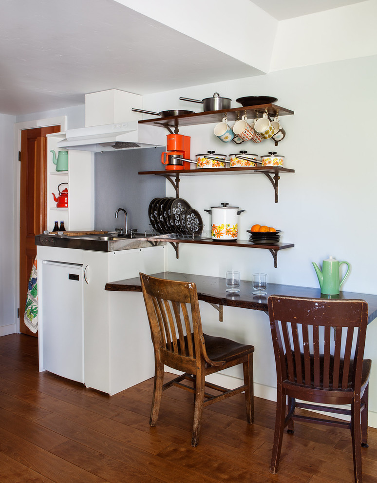 Exempel på ett litet 60 tals linjärt kök och matrum, med en enkel diskho, vita vitvaror, mellanmörkt trägolv, öppna hyllor, vita skåp och bänkskiva i rostfritt stål