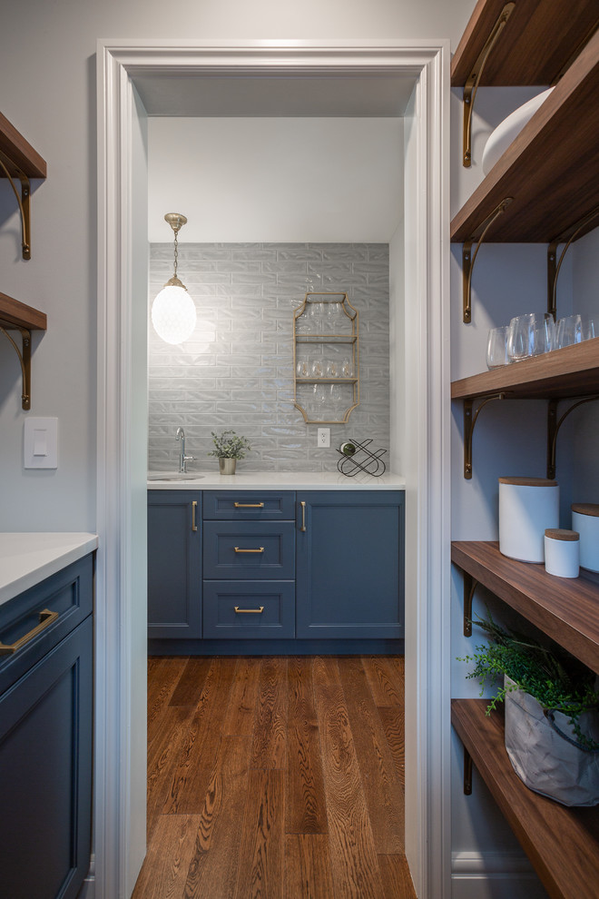 Foto på ett avskilt, mellanstort funkis vit l-kök, med en undermonterad diskho, skåp i shakerstil, blå skåp, vitt stänkskydd, rostfria vitvaror, mellanmörkt trägolv, en köksö och brunt golv