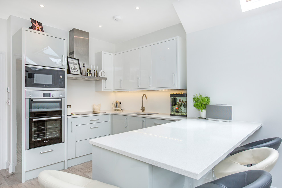 Small contemporary u-shaped kitchen in Other with a submerged sink, flat-panel cabinets and light hardwood flooring.