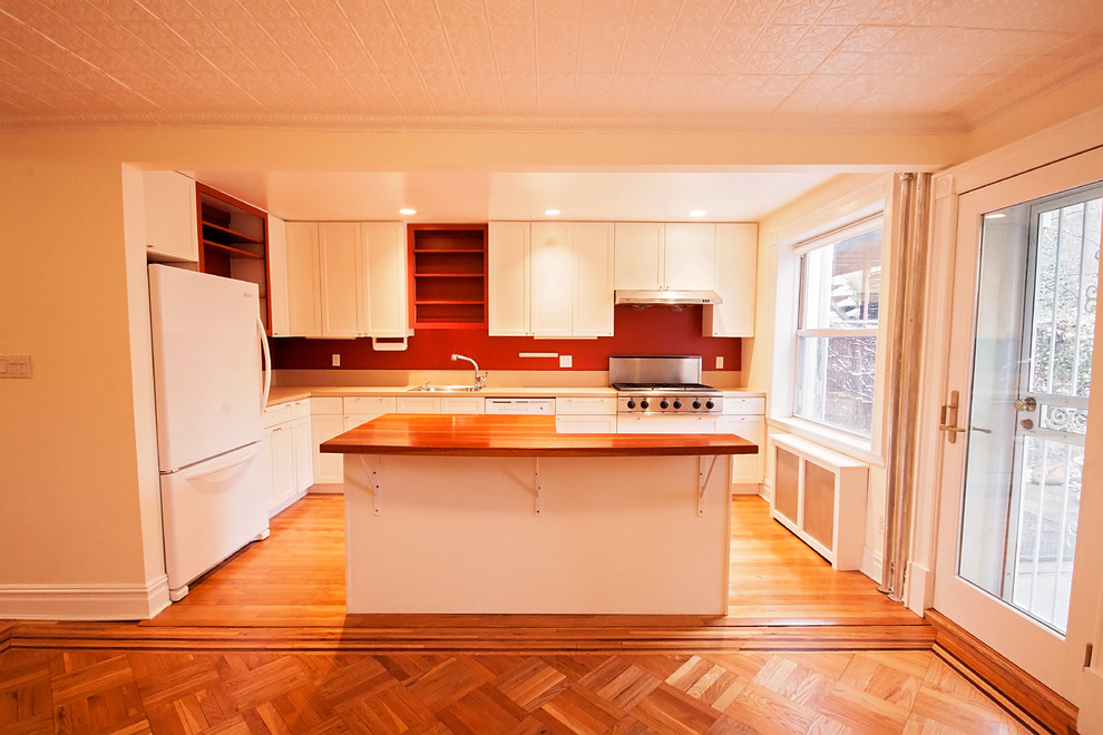 Inredning av ett modernt mellanstort kök, med vita skåp, rött stänkskydd, vita vitvaror, ljust trägolv och en köksö