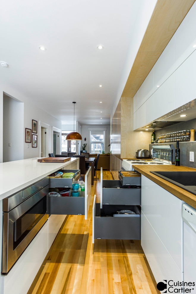Example of a large danish galley light wood floor open concept kitchen design in Montreal with a double-bowl sink, flat-panel cabinets, light wood cabinets, wood countertops, gray backsplash, cement tile backsplash, white appliances and an island