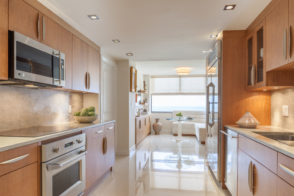 Inspiration for a contemporary galley enclosed kitchen in Miami with a submerged sink, flat-panel cabinets, light wood cabinets, quartz worktops, green splashback, stone slab splashback, stainless steel appliances and porcelain flooring.