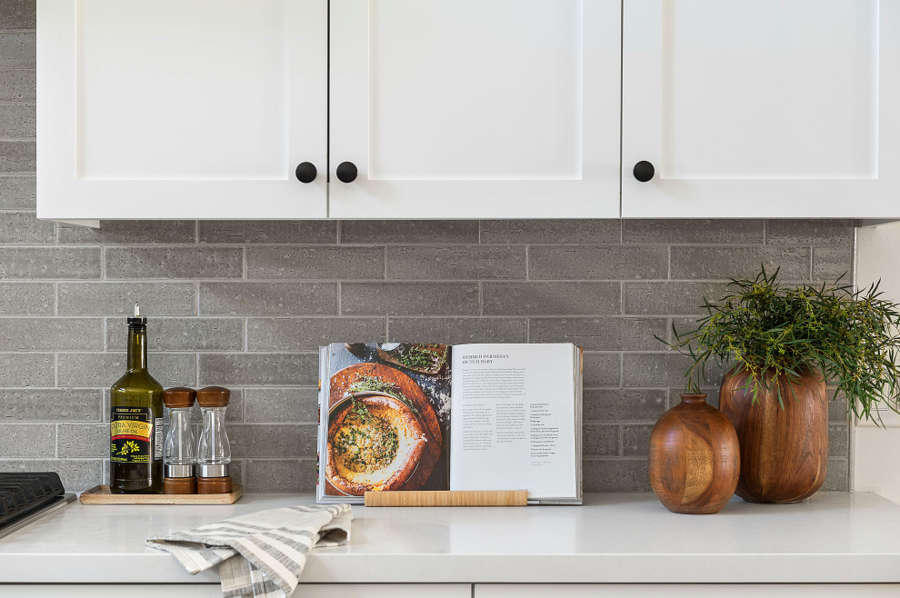 Mid-sized arts and crafts u-shaped porcelain tile and gray floor open concept kitchen photo in San Diego with a farmhouse sink, shaker cabinets, white cabinets, quartz countertops, gray backsplash, ceramic backsplash, stainless steel appliances, an island and white countertops