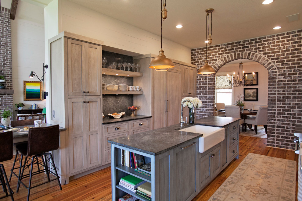 Foto på ett stort lantligt kök, med en rustik diskho, integrerade vitvaror, mellanmörkt trägolv, en köksö, brunt golv, skåp i shakerstil, skåp i ljust trä, bänkskiva i täljsten, brunt stänkskydd och stänkskydd i sten