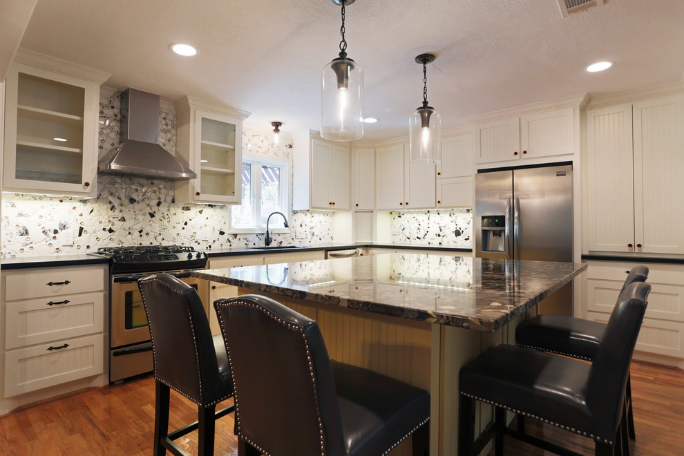 Mid-sized eclectic galley light wood floor eat-in kitchen photo in Houston with a drop-in sink, shaker cabinets, white cabinets, granite countertops, multicolored backsplash, mosaic tile backsplash, stainless steel appliances and an island