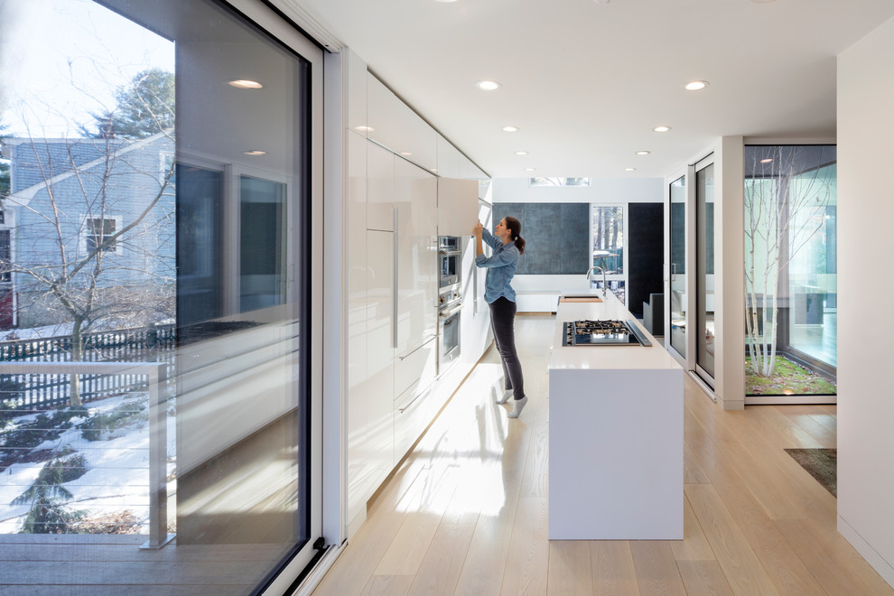 Foto di un cucina con isola centrale moderno con ante lisce, ante bianche, elettrodomestici in acciaio inossidabile, parquet chiaro e pavimento beige