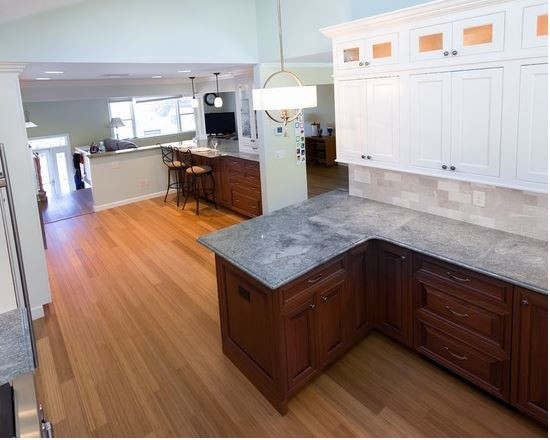 This is an example of an expansive traditional l-shaped kitchen/diner in Providence with a double-bowl sink, beaded cabinets, beige cabinets, granite worktops, beige splashback, marble splashback, stainless steel appliances, bamboo flooring, multiple islands and brown floors.